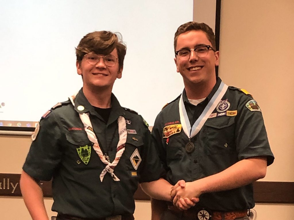 2 Venturers in green field uniforms shake hands at a leadership conference