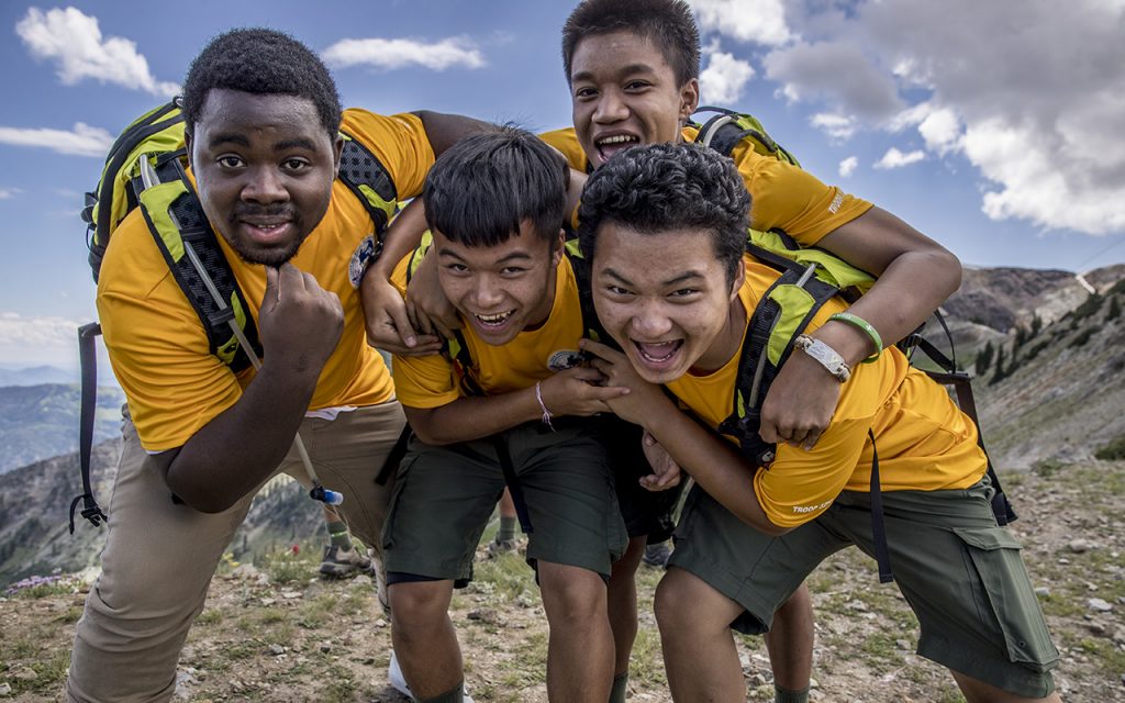 4 teen boys in yellow shirts huddle up and smile to pose for the camera while hiking