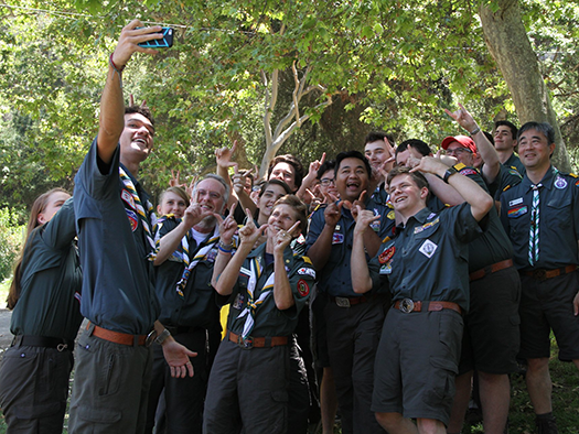 A large group of Venturers in their green field uniforms pose for a group selfie